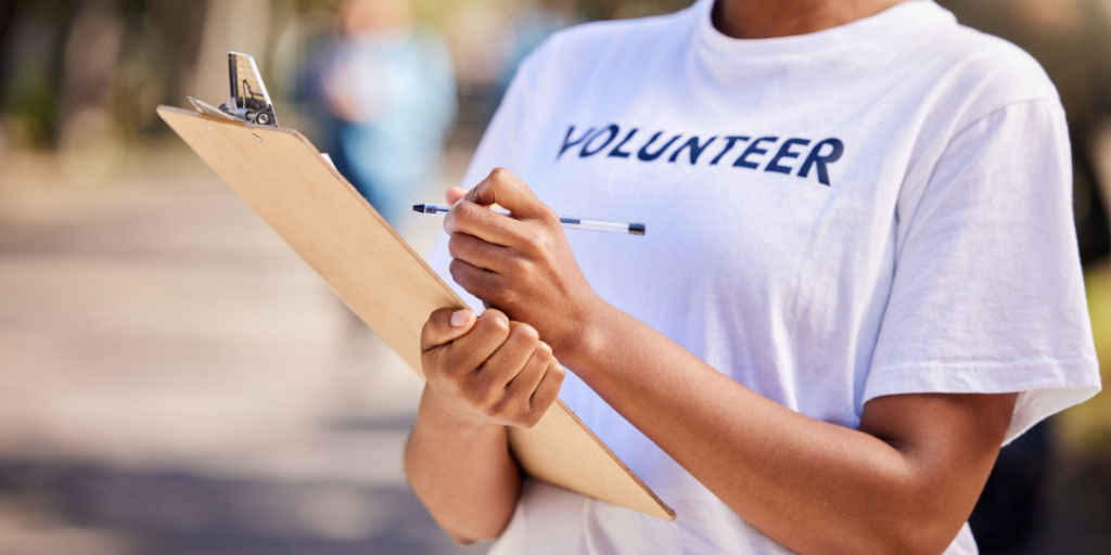 Volunteer in a white volunteer t-shirt holding a clipboard and pen outdoors
