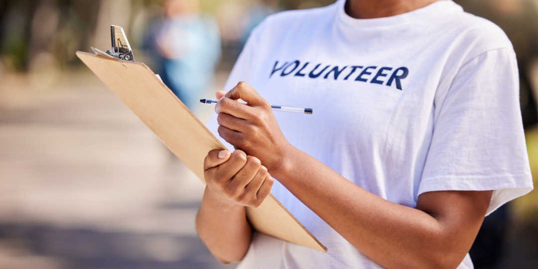 Volunteer in a white volunteer t-shirt holding a clipboard and pen outdoors