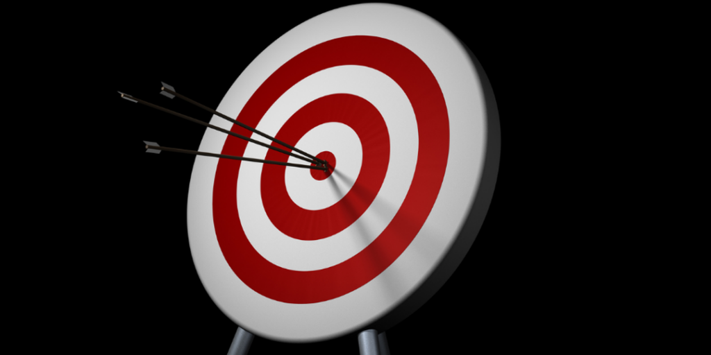 Red and white target with three arrows in the bullseye on a black background