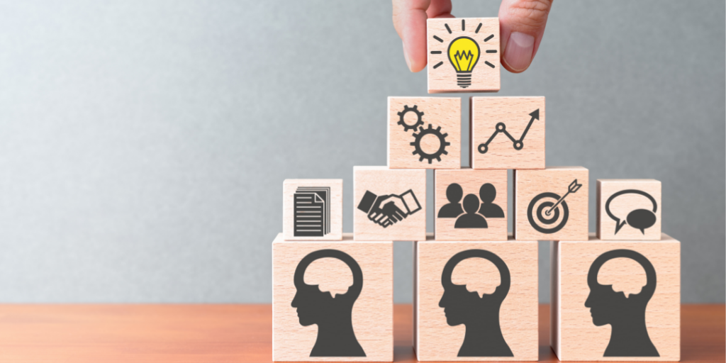 Wooden blocks with icons stacked in a pyramid as a hand places a lightbulb block on top, representing CBT stress management