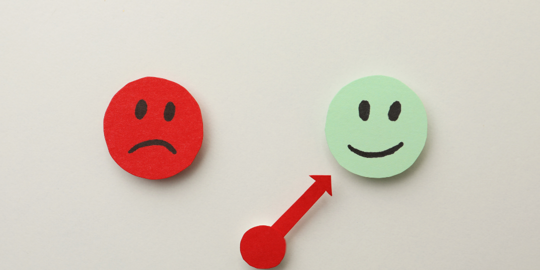 Paper cutouts of a red frowning face and a green smiling face with an arrow between them, representing emotional regulation with DBT