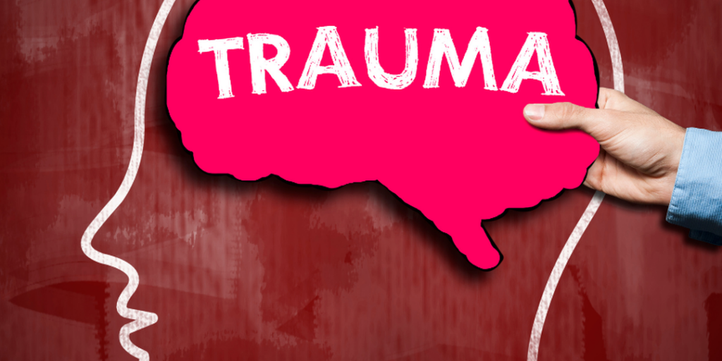 Pink brain-shaped speech bubble labeled TRAUMA held inside a head outline