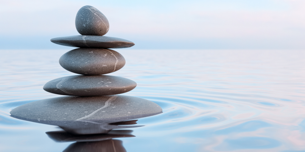 Stack of smooth balanced stones in calm water, representing grounding for trauma recovery